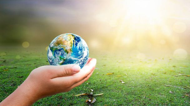 hand holding  Earth on green grass and sunny sky background. Elements of this image furnished by NASA - Foto, Bild