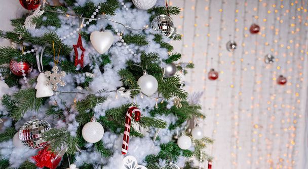 Decorated Christmas tree in the room. Coniferous tree with white and red baubles located near the white wall during the celebration of the holiday. - Fotoğraf, Görsel
