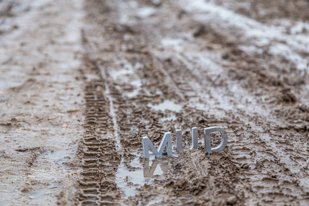 het woord modder bestaande uit zilvermetalen letters op nat vuil oppervlak - Foto, afbeelding