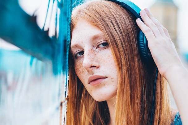 Portrait of beautiful ginger, teen girl listening to music, headphones on her head. - Foto, Bild