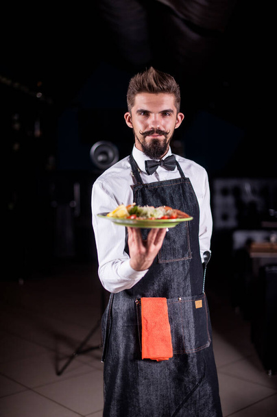 Angestellter eines Whisky-Restaurants serviert gekochtes Gericht auf schwarzem Hintergrund. - Foto, Bild