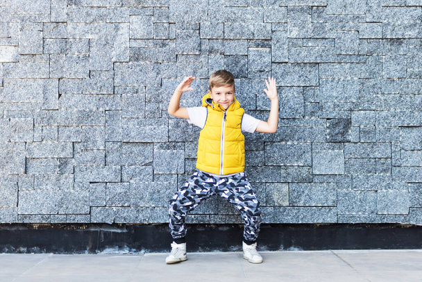 Szczęśliwy dzieciak bawiący się tańcząc pod ścianą. Przestrzeń kopiowania.  - Zdjęcie, obraz