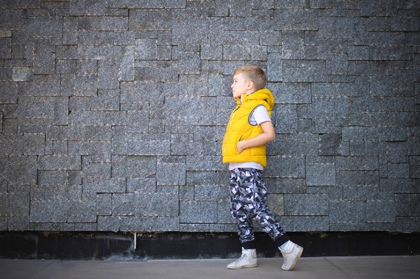 Longitud completa de niño pequeño caminando con las manos en los bolsillos contra la pared. Copiar espacio.  - Foto, Imagen