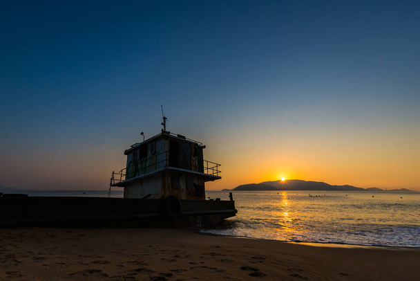 ベトナムのKh á nh H ò a省のNha Trangでの美しい黄金の日の出の間のビーチでの古いボート. - 写真・画像