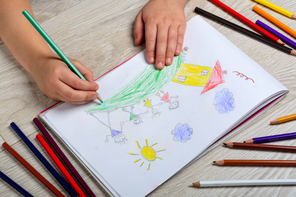 El niño dibuja a su familia en un pedazo de papel con lápices de colores. ¿Qué puede decir la foto de un niño? El concepto de psicología infantil - Foto, Imagen