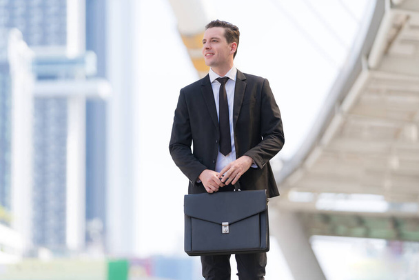 Succesvolle zakenman op zakenvergadering met aktetas lopend voor modern kantoor - Foto, afbeelding