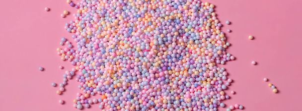 Haufen pastellfarbener Kugeln auf rosa. Styropor oder Polystyrolschaum Hintergrund. Mischung aus bunten Zuckerbällchen, die zum Dekorieren von Backwaren und Süßigkeiten verwendet werden. Regenbogenfarbene Zuckerchips, Dragee-Spins, Süßwaren. - Foto, Bild