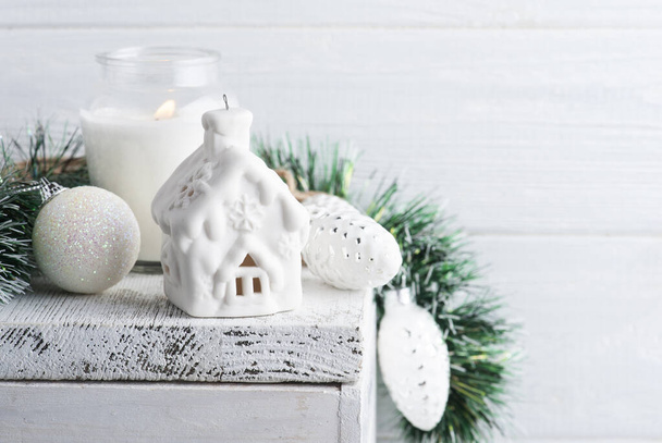 Christmas decoration with toy house and lit candle on white rustic background. Copy space for greeting - Foto, Imagem