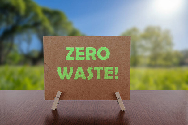 Zero waste text on card on the table with sunny green park background. Ecology concept, recycle, reuse, reduce waste. - Photo, image