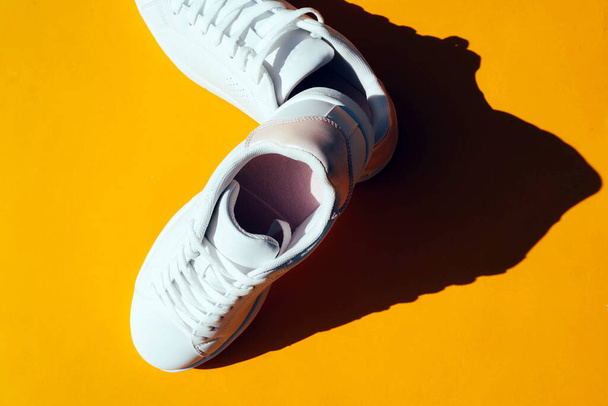 White sneakers on an orange background with hard shadows. Stylish sports shoes. - Photo, Image