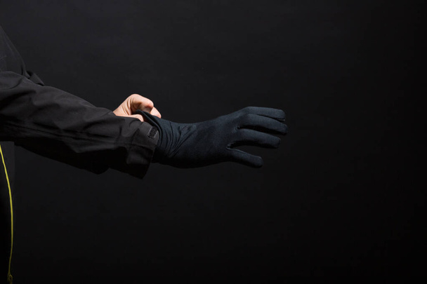 Hand in zwarte handschoenen van een misdaad op een zwarte achtergrond. Handschoenen worden op de hand gedragen. De man doet een zwarte handschoen om zijn hand.. - Foto, afbeelding