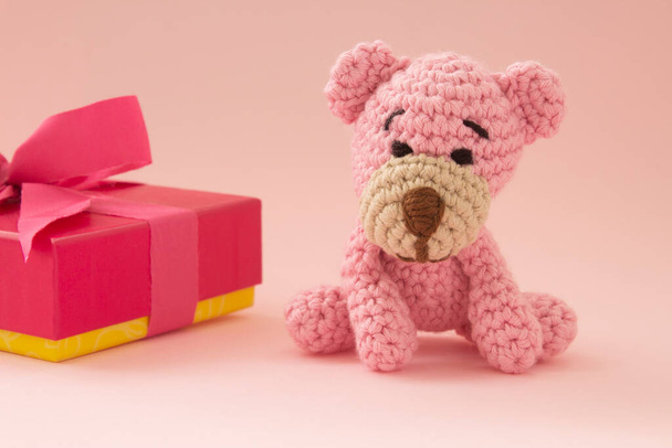 Невеликий гачком ведмідь рожевого кольору з подарунковою коробкою на спині. Рожевий колір. Концепція кохання
. - Фото, зображення