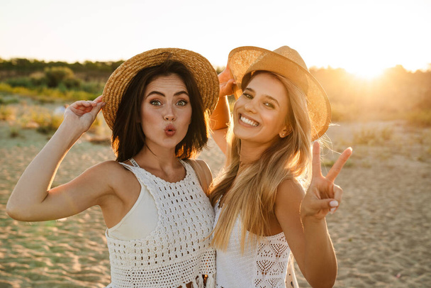 Two young caucasian happy women smiling and gesturing peace sign while walking outdoors - Fotó, kép