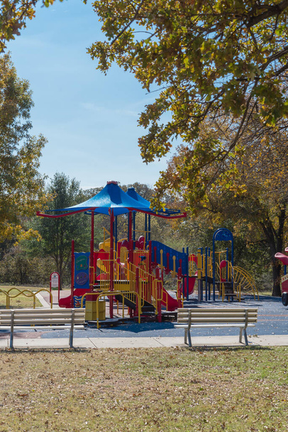 Widok z tyłu dwóch pustych ławek patrząc na kolorowy plac zabaw z jesiennymi liśćmi w Kwiat Kopiec, Teksas, USA - Zdjęcie, obraz