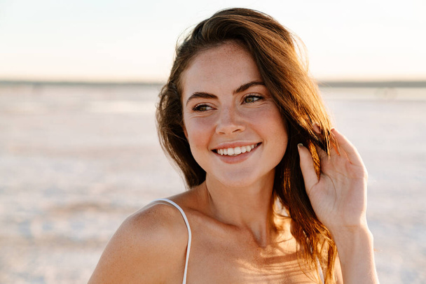 Photo of a cheerful young pretty girl walking outdoors at the beach - Foto, afbeelding