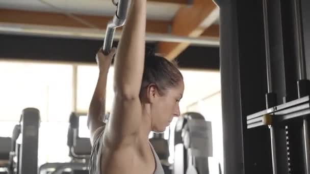 Krásná mladá žena ve sportovních trenýrkách a šedý tank top zapojený do fitness v tělocvičně potřásá rukou na speciální simulátor - Záběry, video