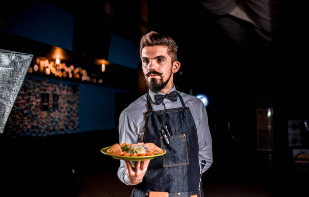 Cameriere amichevole professionale porta piatto appetitoso su uno sfondo nero. - Foto, immagini