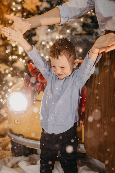 Child boy has a fun near his mother, retro car and Christmas tree with decorations against background of falling snowflakes. - Zdjęcie, obraz
