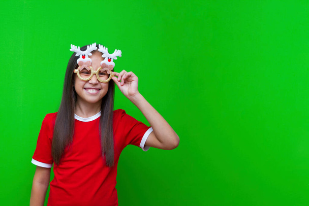 Χαρούμενο κορίτσι με σκούρα μαλλιά σε κόκκινο μπλουζάκι και αστεία γυαλιά για Χριστούγεννα και Πρωτοχρονιά. - Φωτογραφία, εικόνα