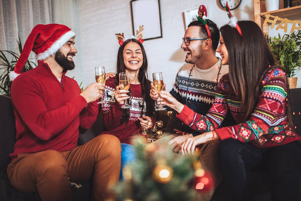 Grupo de amigos sentados en una casa bien decorada, divirtiéndose mientras celebran la Navidad o el Año Nuevo - Foto, imagen