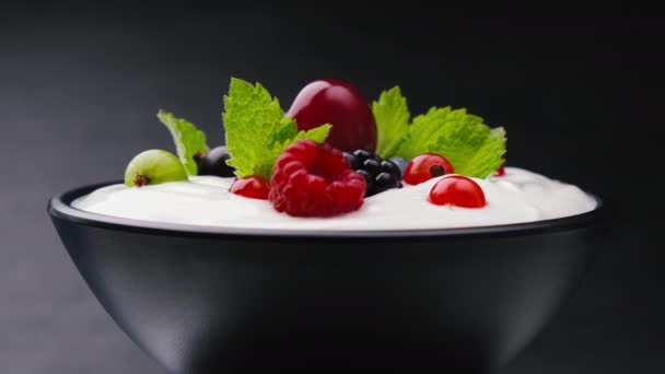 Cuenco de yogur con bayas silvestres sobre fondo negro - Imágenes, Vídeo