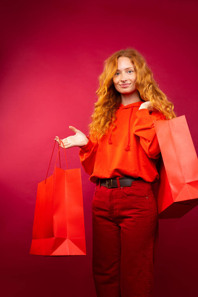  A beautiful girl, all in red with large gift bags, posing against a red background. Holiday concept. High quality photo - Foto, Bild