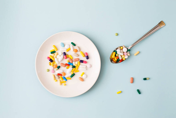 Creative medical layout made with colorful pills, capsules and supplements on white plate on light blue background. Minimal modern pharmacy or health care concept. Flat lay, top view, copy space - Fotografie, Obrázek