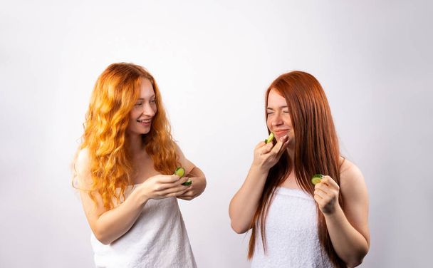 The girls laugh and put pieces of cucumber on their faces. Photo on a white background. Spa and cosmetology concept. High quality photo - Foto, afbeelding