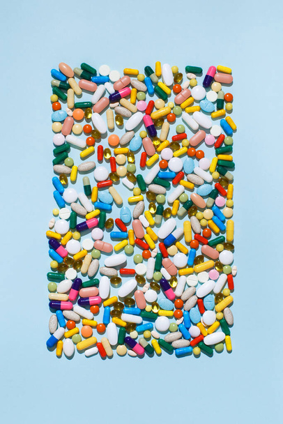 Creative layout of colorful pills and capsules on blue background with summer sun and sharp shadow. Minimal medical concept. Pharmaceutical, Covid-19 or Coronavirus. Flat lay, top view. - Foto, afbeelding