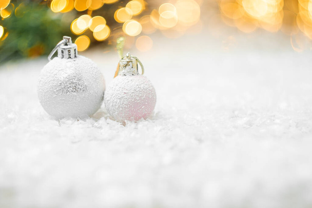 Decorative Christmas balls laying in a snow with yellow lights bokeh on the background. Greeting card for New Year holidays or party with copy space. - Photo, image
