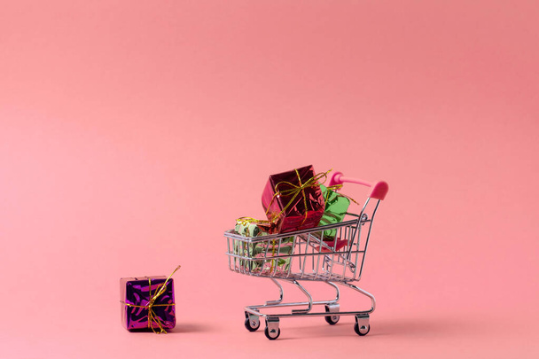 shopping trolley full of present boxes copy space, shopping concept poster on a pink background - Foto, afbeelding