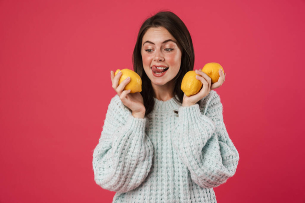 Image of happy beautiful girl posing with arms lemons isolated over pink background - Foto, imagen