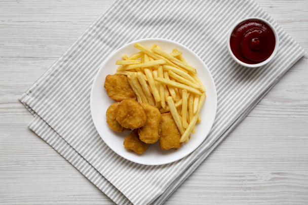 Comida rápida sabrosa: Nuggets de pollo y papas fritas en un plato sobre un fondo de madera blanca, vista superior. Acostado plano, arriba, desde arriba.  - Foto, Imagen