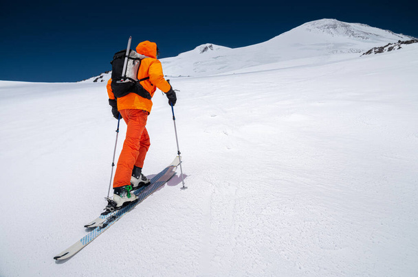 A mountaineer skier with a backpack, an ice ax, skis and poles, ascend on a ski tour to Mount Elbrus. Backcountry and freeride skiing concept - Photo, Image
