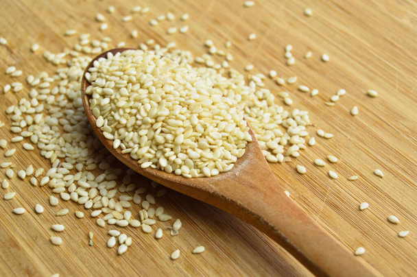 Organic fresh raw sesame seeds, in wooden spoon on bamboo cutting board - Photo, Image