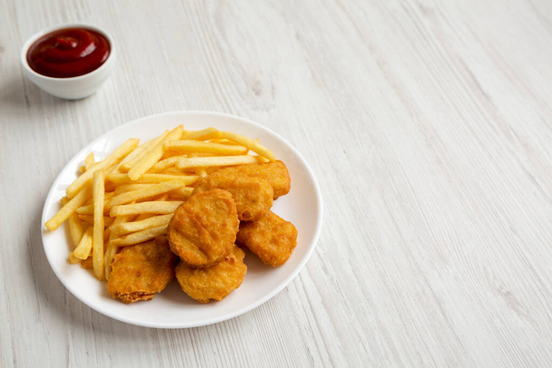Comida rápida sabrosa: Nuggets de pollo y papas fritas en un plato sobre un fondo de madera blanca, vista de ángulo bajo. Copiar espacio. - Foto, Imagen