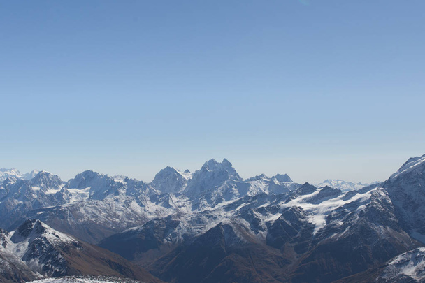 Snowy peaks of the Caucasus mountain range against a blue sky. - Фото, изображение
