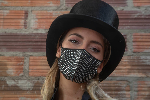 Молода жінка носить блискучу чорну маску для обличчя на цегляній стіні
 - Фото, зображення