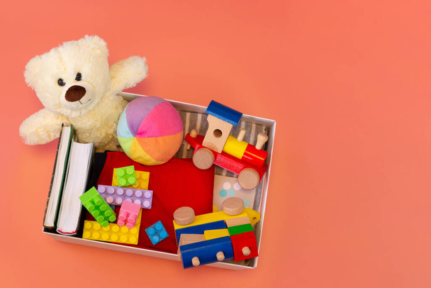 İçinde oyuncaklar, kitaplar, pembe arka planda yardım amaçlı kıyafetler olan bağış kutusu. Üst görünüm - Fotoğraf, Görsel