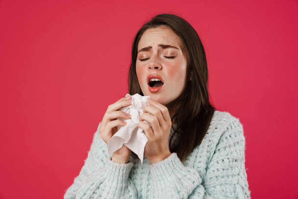 Image of unhappy beautiful girl sneezing in napkin due to flu isolated over pink background - Foto, immagini