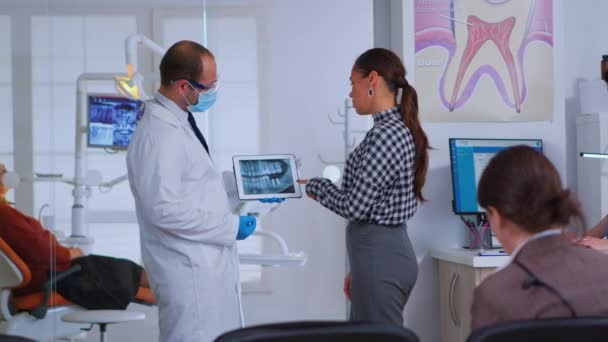 Стоматолог в приемной говорит с пациенткой о рентгене - Кадры, видео