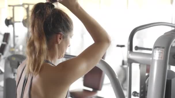 Όμορφη νεαρή γυναίκα στο γυμναστήριο σφίγγει το χέρι σε ένα ειδικό προσομοιωτή - Πλάνα, βίντεο