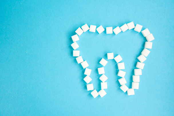 Sugar cubes are laid out in the form of a tooth on blue background. - Foto, Bild