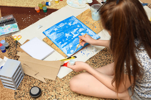 meisje tekent thuis, artistieke creatie, maakt creatieve kunstwerken van papier, verf en penselen - Foto, afbeelding