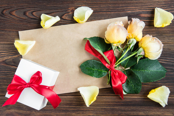 Sárga rózsák piros masnival és üdvözlőkártyával fából készült háttérrel. Női nap. Valentin nap. Születésnap. - Fotó, kép