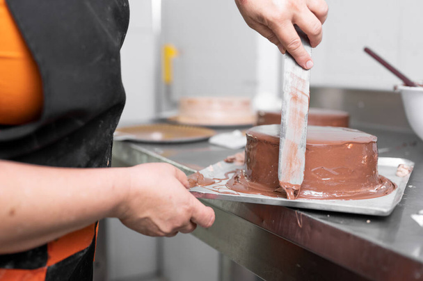 Donna pasticciera finitura torta al cioccolato con glassa, fase finale di cottura. Il processo di fabbricazione della torta al cioccolato. - Foto, immagini