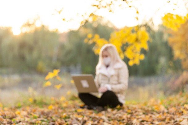 Życie podczas covid-19. Młoda kobieta w masce ochronnej na laptopie w parku publicznym. Stylowa kobieta korzystająca z komputera podczas pracy na zewnątrz. Nauka na odległość i praca zdalna podczas pandemii - Zdjęcie, obraz