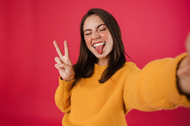 Image of joyful girl gesturing peace sign while taking selfie photo isolated over pink background - Fotografie, Obrázek
