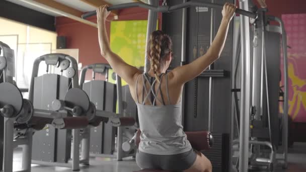 Άποψη από πίσω της όμορφης νεαρής γυναίκας με αθλητικό σορτς και γκρι μπλουζάκι που ασχολείται με την φυσική κατάσταση στο γυμναστήριο σφίγγει το χέρι σε έναν ειδικό προσομοιωτή - Πλάνα, βίντεο