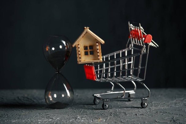Model van huis, trolley en zandloper. Besparen en kopen van een vastgoedconcept - Foto, afbeelding
